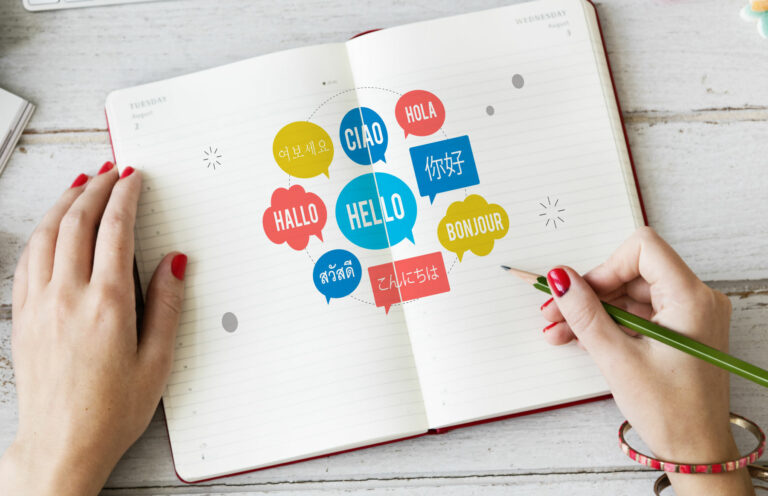 L’image montre un carnet ouvert avec une illustration colorée de bulles de dialogue contenant des salutations dans différentes langues.