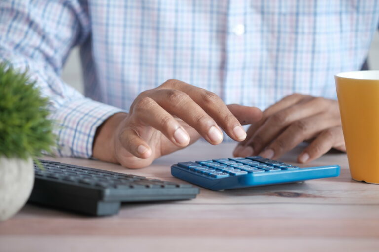 L'image montre une personne en train de taper sur une calculatrice pour faire sa comptabilité ou sa gestion financière.